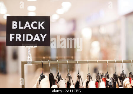 Background image of BLACK FRIDAY sigh on rack with clothes on sale in shopping mall, copy space Stock Photo