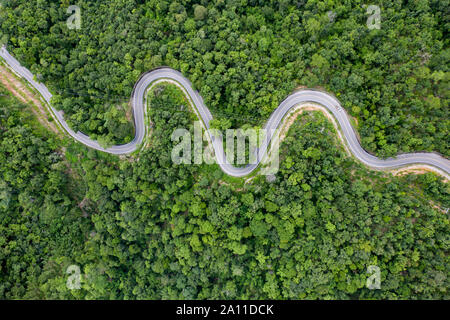 Aerial view of countryside road passing through the green forrest and mountain. Stock Photo