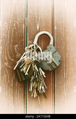 A bunch of old keys and two locks hang on a nail driven into a wooden wall. Vintage. Stock Photo