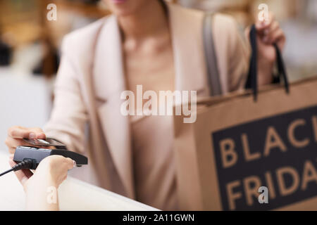 Close up of unrecognizable woman paying via NFC while buying clothes in shopping mall during sale season, copy space Stock Photo