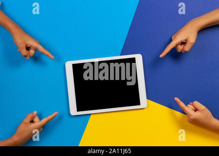 Kids hands holding white tablet computer on light blue, yellow and blue background Stock Photo