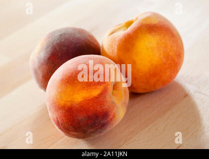 Three peaches on a wooden surface Stock Photo