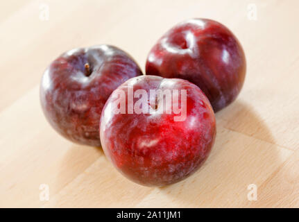 Three plums on a wooden surface Stock Photo