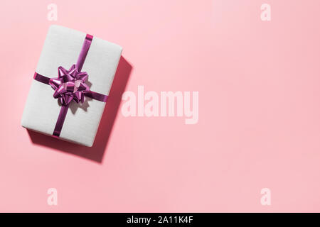 Christmas white giftbox with bow on pink surface. Space for wishes. Xmas card. Boxing day. View from above. Stock Photo