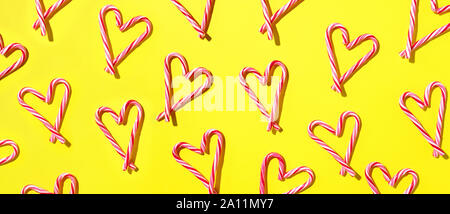 Pattern with hearts made of Christmas candy canes on yellow background. Top view. Flat lay. Love, Valentines day concept. New year and Christmas card. Stock Photo