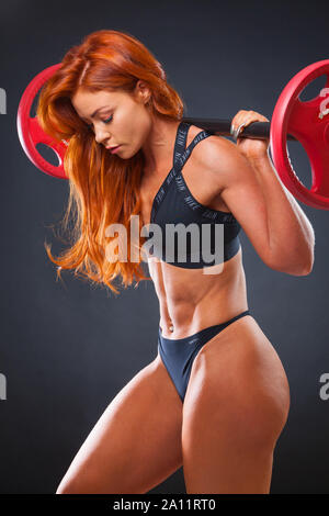 A young red haired female fitness model showing her muscles in a studio setting with black background Stock Photo