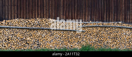 Panorama - Large pile of wood in front of a wooden barn wall Stock Photo