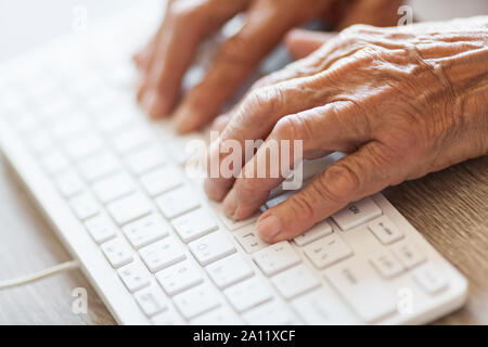 Elderly woman typing on a PC keyboard Stock Photo