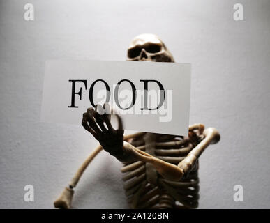 Skeleton holding a Food tag label implying lack of food Stock Photo