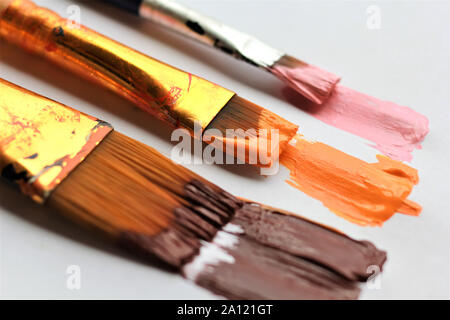 Three brushes of different size leaving acrylic paint brown orange pink strokes on white paper Stock Photo