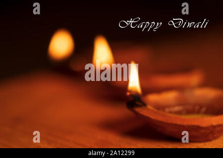 Beautiful blurred background stock photo of Diwali Diya or oil clay lamp with Happy Diwali text and copy space isolated on black background. Stock Photo