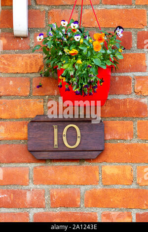 House number 10 on a simple wooden sign on a red brick wall with a flower pot Stock Photo