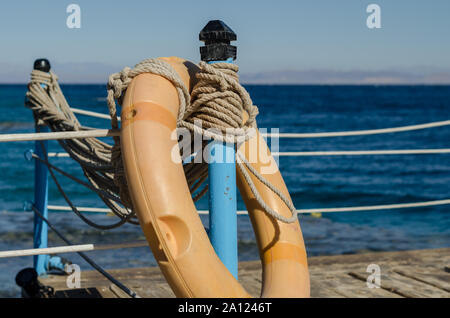 orange lifebuoy on a wooden table with ropes on a wooden platform on a background of blue sea close up Stock Photo