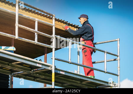 man on scaffolding installing new wooden planks on house roof eaves Stock Photo