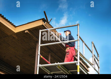 old house renovation - construction worker installing new planks on house roof eaves Stock Photo