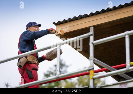 man on scaffolding painting house roof planks with paint roller Stock Photo