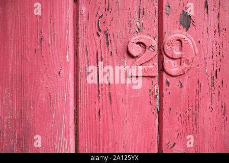 Rustic aged closeup of wood panel painted with red chipping colour.  Vertical slats with vertical wood lines texture and metal number 29 over painted Stock Photo