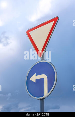Give way and turn left, against the backdrop of dramatic sky and clouds. Stock Photo