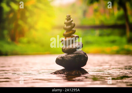 Close-up abstract image of wet rough natural brown uneven different sizes and forms stones balanced like pyramid pile landmark in shallow water on Blu Stock Photo