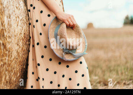 Young woman holding straw hat in wheat field. Agriculture background with copy space. Summer and autumn harvest concept. Harvested field with straw ba Stock Photo