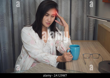 Asian woman in white satin nightgown with hard headache holding. Female is suffering from a headache Stock Photo