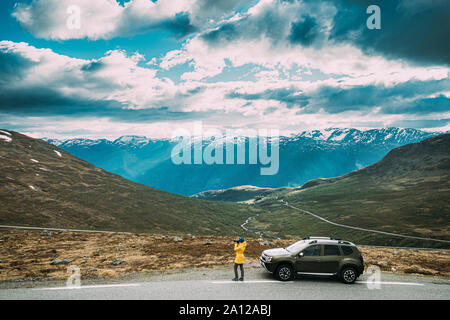 Aurlandsfjellet, Norway. Young Caucasian Woman Lady Tourist Traveler Photographer Taking Pictures Photos Near Parked Car. Aurlandsfjellet Scenic Route Stock Photo