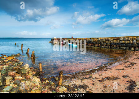 A small boat moored at an old stone jetty at Sannox on the Isle of Arran in Scotland Stock Photo