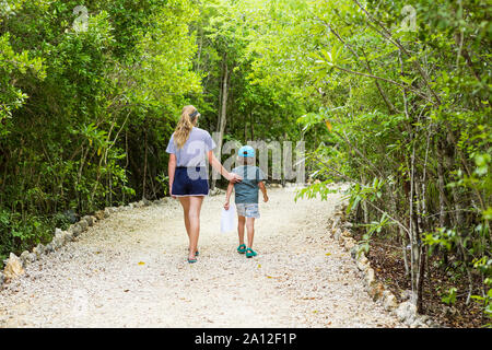 rear view of 13 year old sister and her 5 year old brother walking on nature path Stock Photo