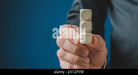 Hand of a businessman holding a stack of three blank wooden dices. Over navy blue background with copy space. Stock Photo