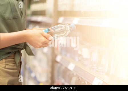 Girl choosing bottle of drinking water in grocery section of supermarket. Copy space. Water balance and body hydration. Healthy diet concept. Sustaina Stock Photo