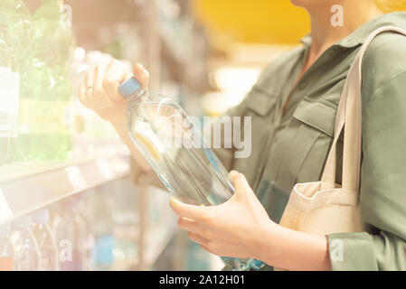 Girl choosing bottle of drinking water in grocery section of supermarket. Copy space. Water balance and body hydration. Healthy diet concept. Sustaina Stock Photo