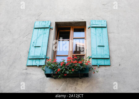 Colorful painted turquoise shutters on a window with geraniums in the medieval town of Yvoire, Haute-Savoie, Auvergne-Rhône-Alpes, France. Stock Photo