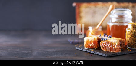 Honeycomb and honey jar with dipper on black slate tray over dark backdrop. Copy space. Top view Stock Photo