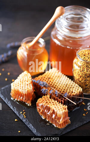 Honeycomb and honey jar with dipper on black slate tray over dark backdrop. Copy space. Top view Stock Photo