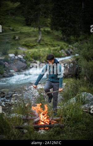 Young man making fire while camping outdoors, in an alpine wilderness Stock Photo