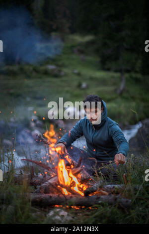 Young man making fire while camping outdoors, in an alpine wilderness Stock Photo