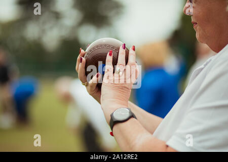 A close up shot of a senior woman holding a bocce ball, ready to take her shot. She is wearing nail polish and a watch. Stock Photo