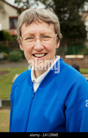A portrait of a senior woman smiling at a bowling green. He is wearing glasses. Stock Photo