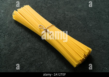 Raw spaghetti pasta tied with a rope on a black texture background. Copy space. Stock Photo