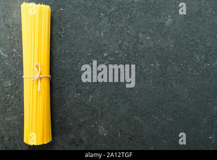 Raw spaghetti pasta tied with a rope on a black texture background. Copy space. Stock Photo