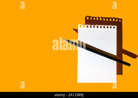 a blank sheet of Notepad, black pencil and hard shadows on a bright yellow background Stock Photo