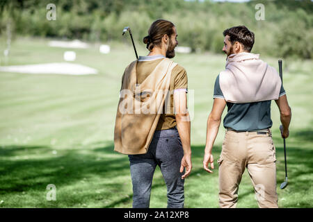 Two male best friends walking with golf equipment on beautiful playing course, talking and having fun during a game, rear view Stock Photo