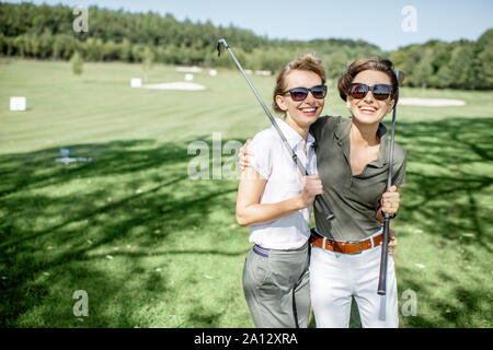 Portrait of a two female best friends standing with golf equipment on a playing course, talking and having fun during a game on a sunny day Stock Photo