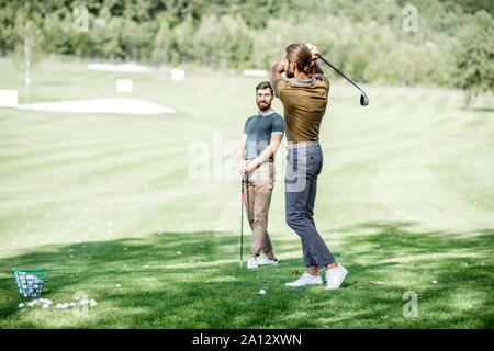 Two male friends playing golf on the golf course, man swinging a putter Stock Photo