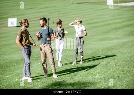 Group of friends talking and walking with putters during the golf play on the beautiful course on a sunny day Stock Photo