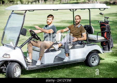 Two male best friends having fun while driving a golf car on the playing course on a sunny day Stock Photo