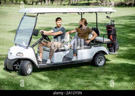 Two male best friends having fun while driving a golf car on the playing course on a sunny day Stock Photo