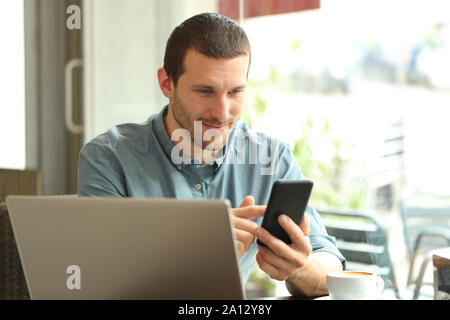 Man using smart phone and laptop sitting in a coffee shop Stock Photo
