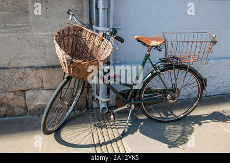 An old, worn bicycle with a wicker basket in front is parked against a wall in the city. Stock Photo