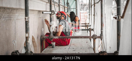 Two workers stands high on the scaffolding, plastering and renovating the wall on the old utility building Stock Photo